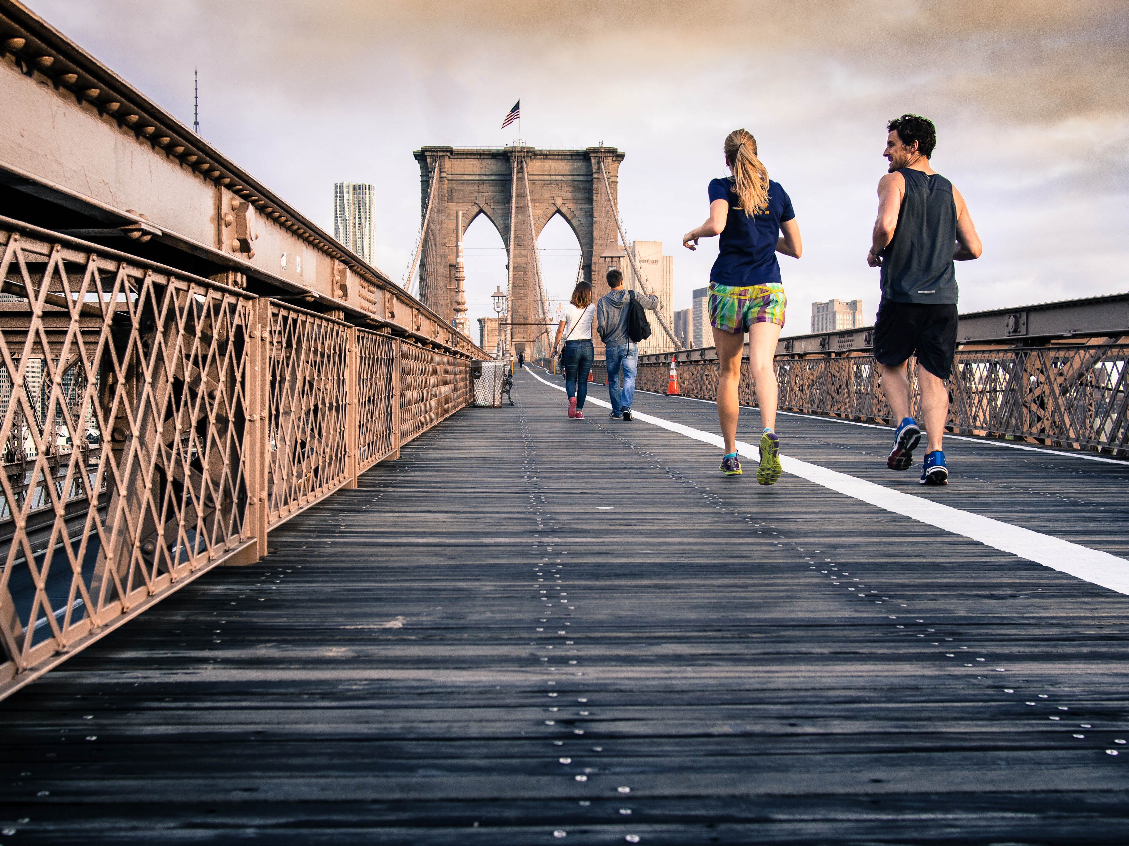 Two runners moving along the Brooklyn Bridge pedestrian promenade in morning light